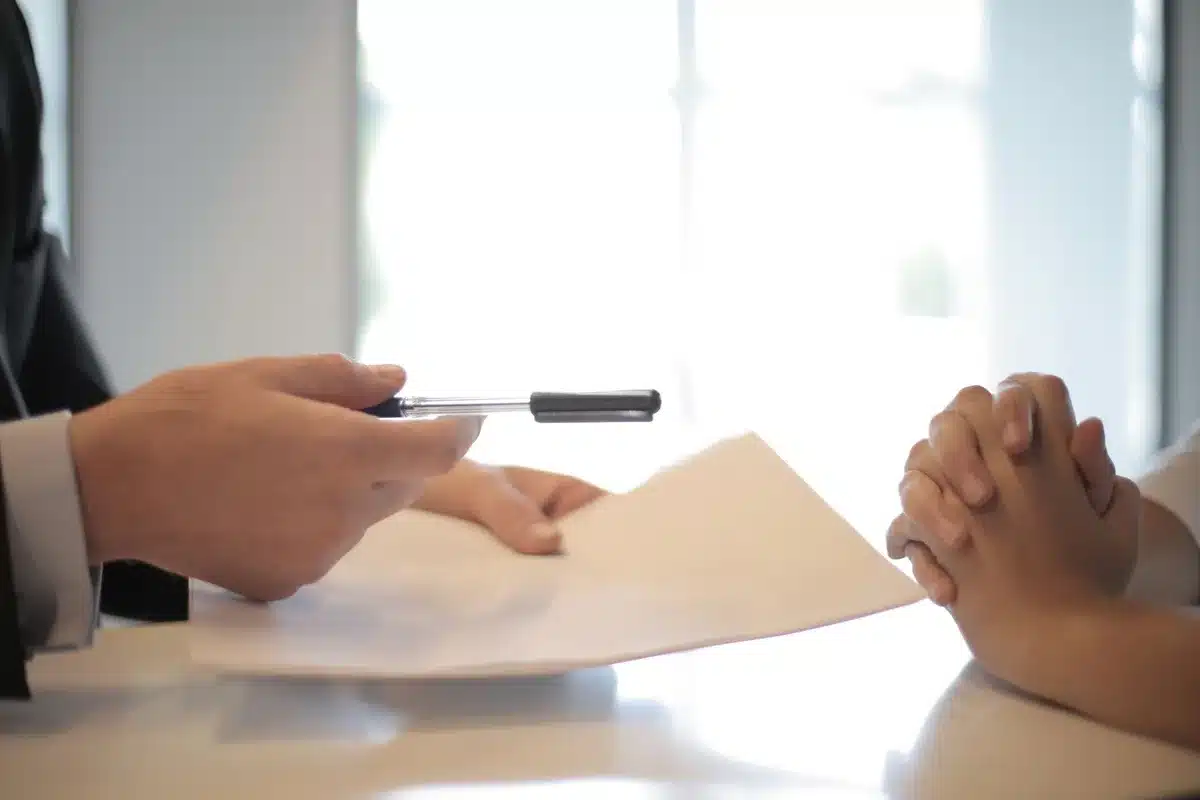 Personne anonyme triant des documents d'assurance habitation à une table, lumière du jour