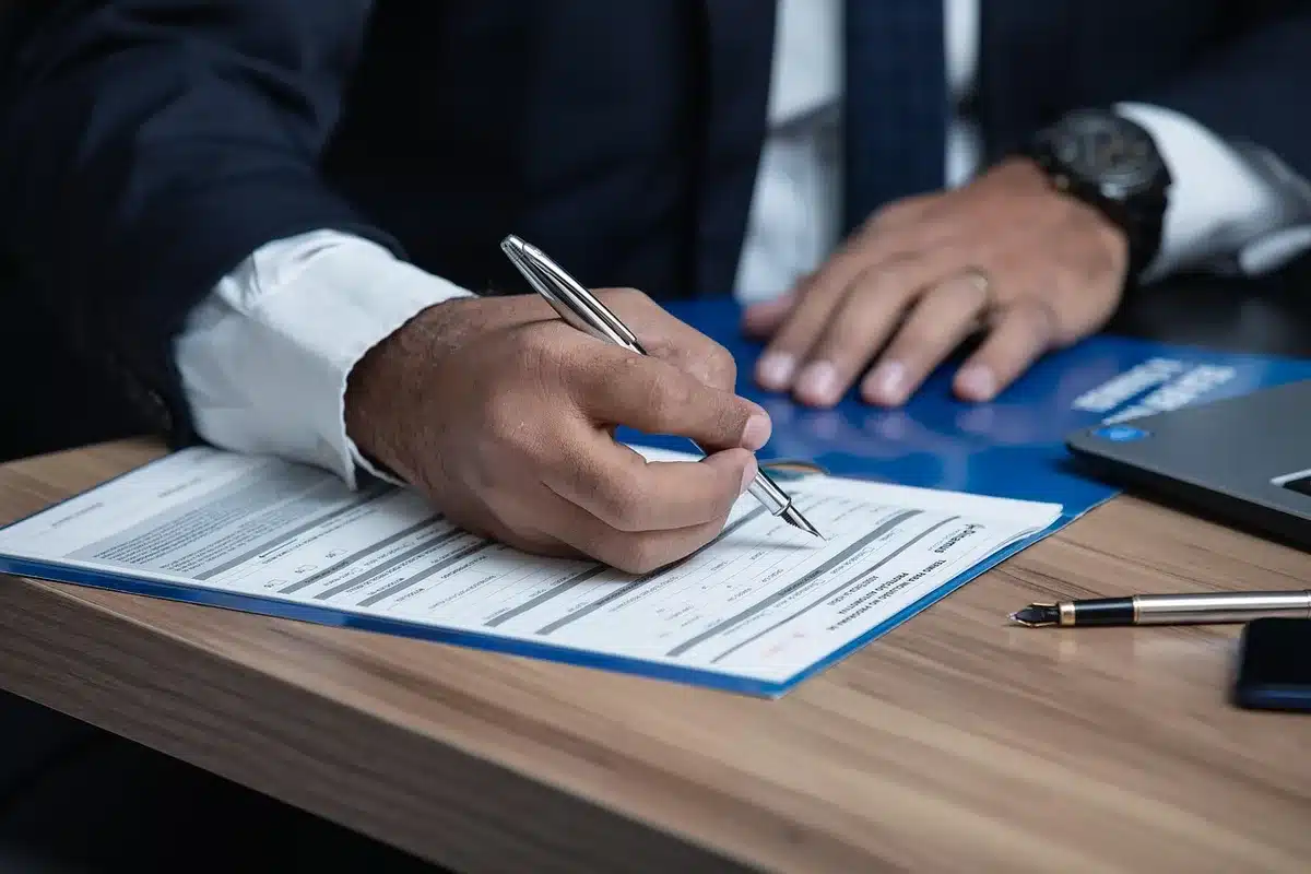 Personne signant des documents de prêt immobilier sur un bureau en lumière du jour